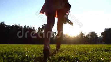 年轻<strong>女孩</strong>赤脚走在草地上，手里<strong>拿</strong>着她的鞋子，4K<strong>放大镜</strong>头。 橙色日落色彩